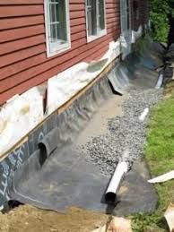 Black landscape fabric and gravel drainage along a red house foundation with white trim.