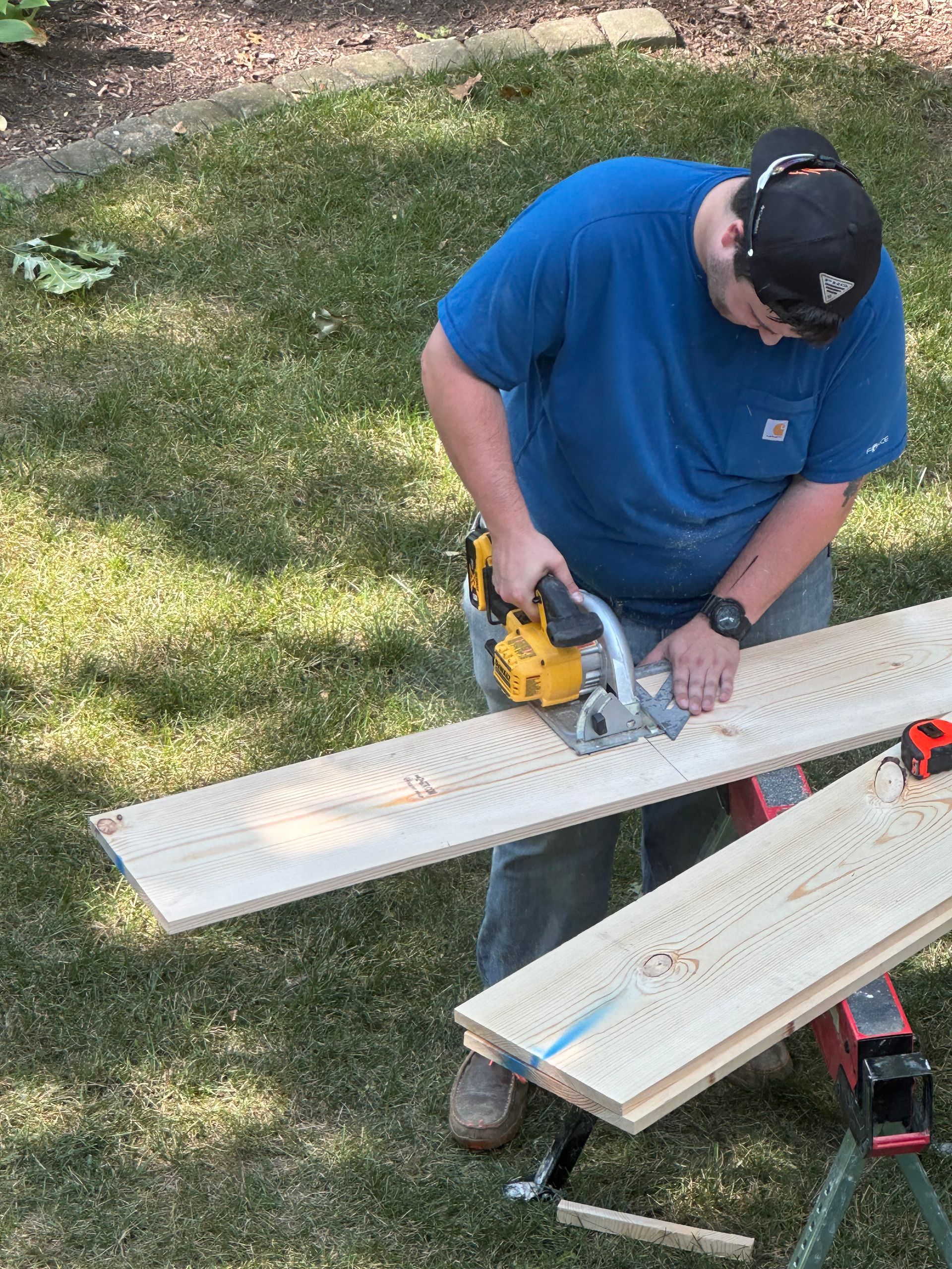 Person using a circular saw to cut a white board outdoors on sawhorses