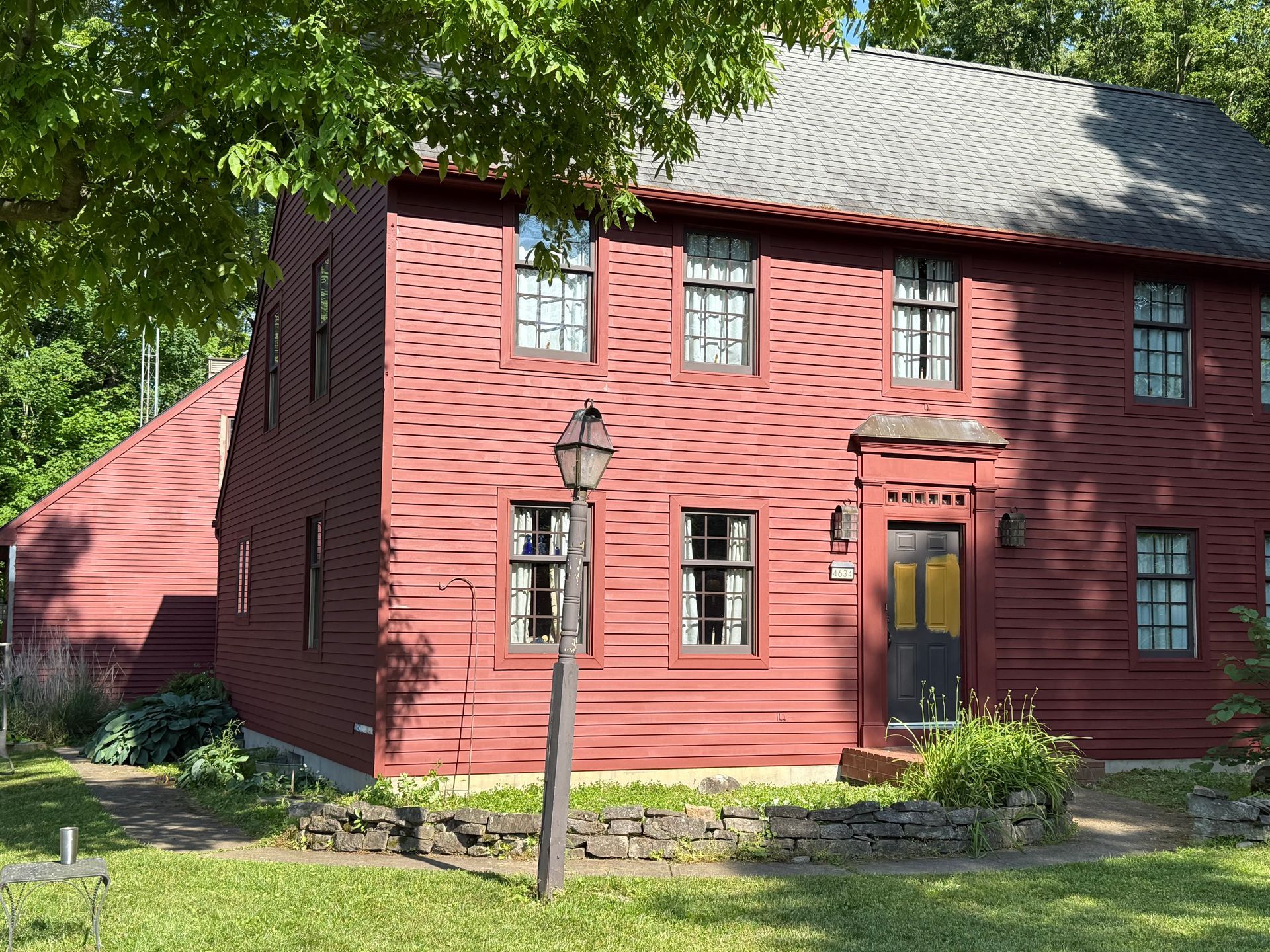 Red wooden house with white-trimmed windows and a lantern post in a leafy yard.