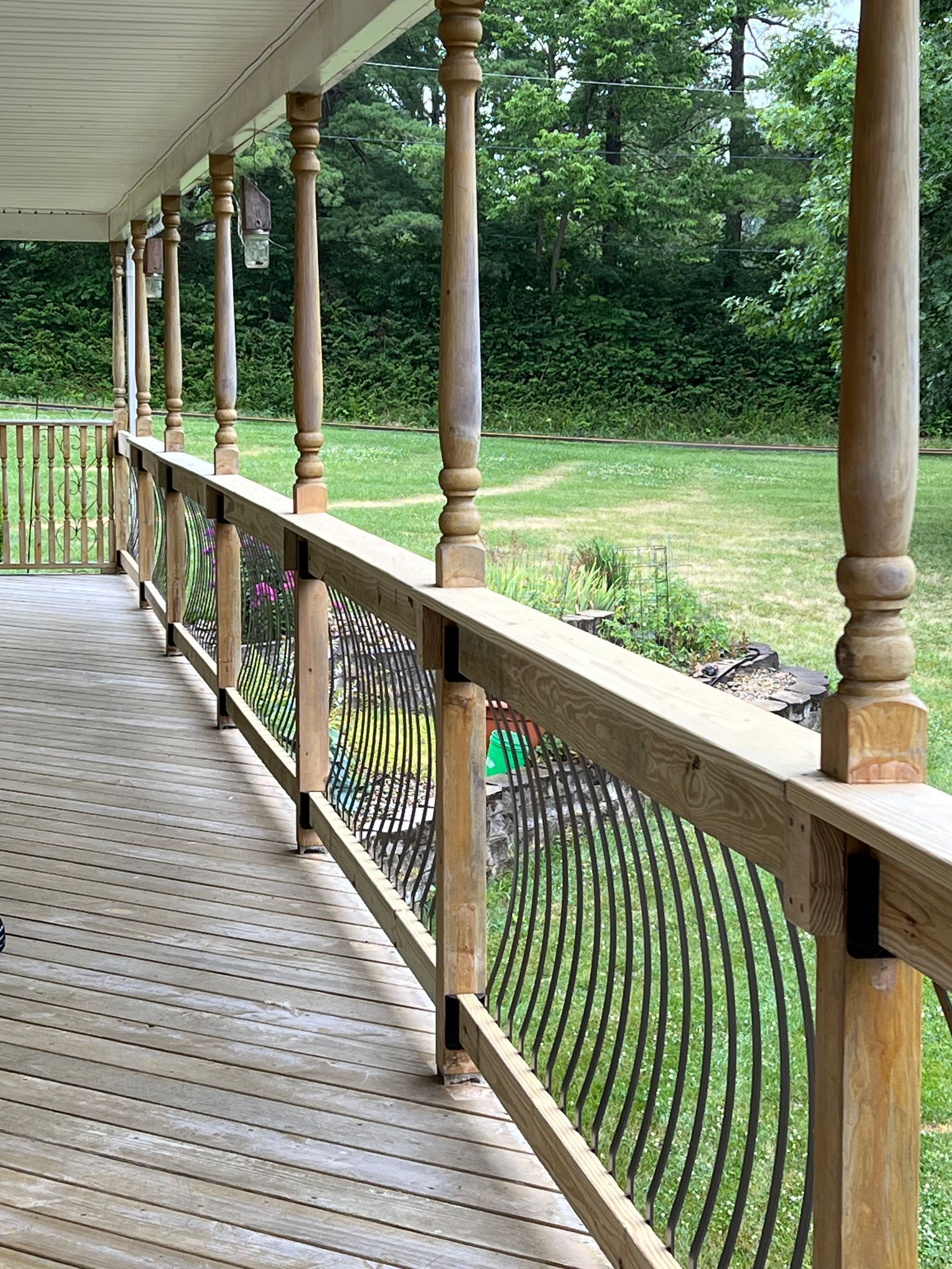 Wooden porch with railing overlooking a green yard and trees