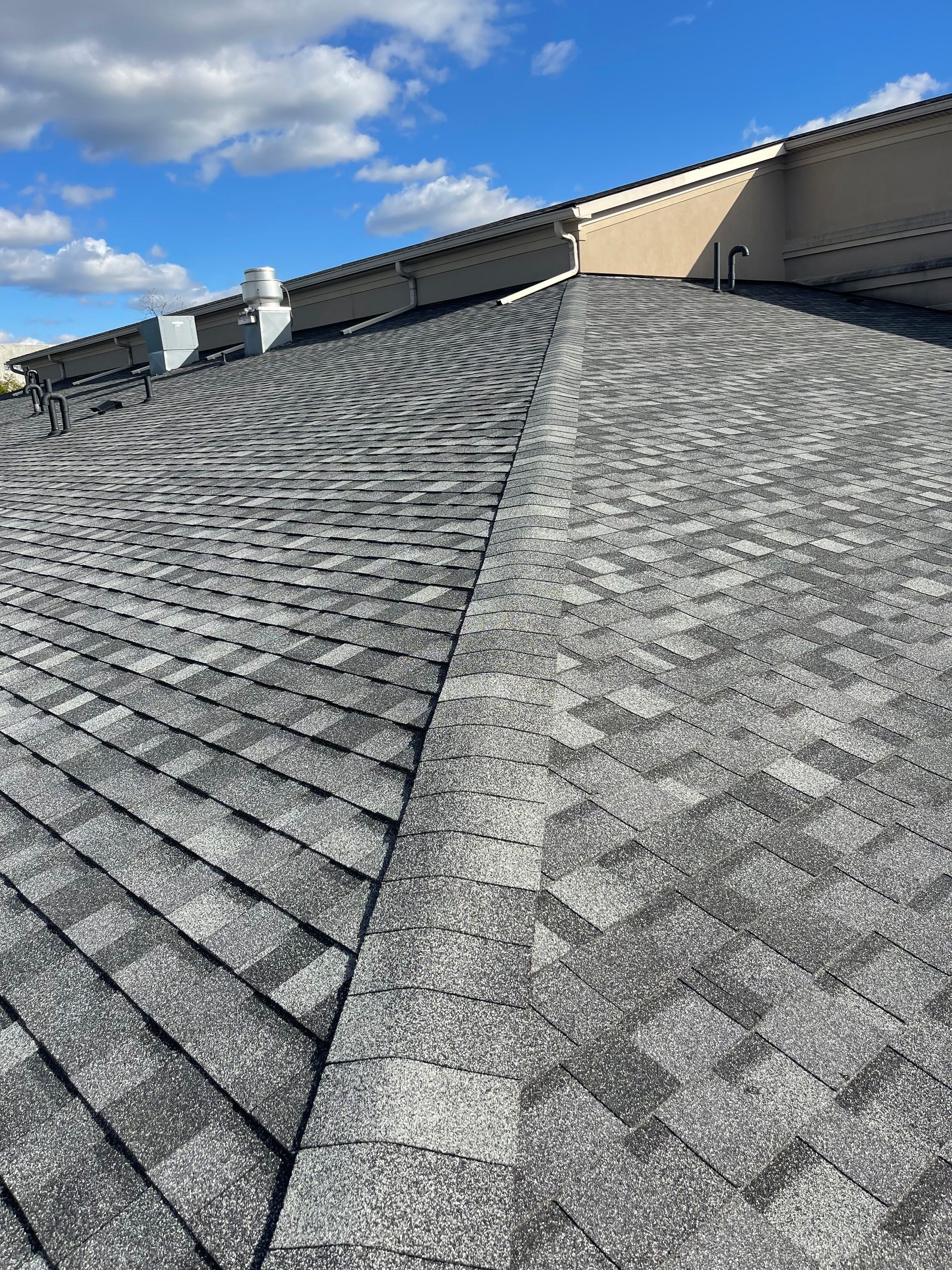 Gray shingle roof with a ridge line under a blue sky with clouds