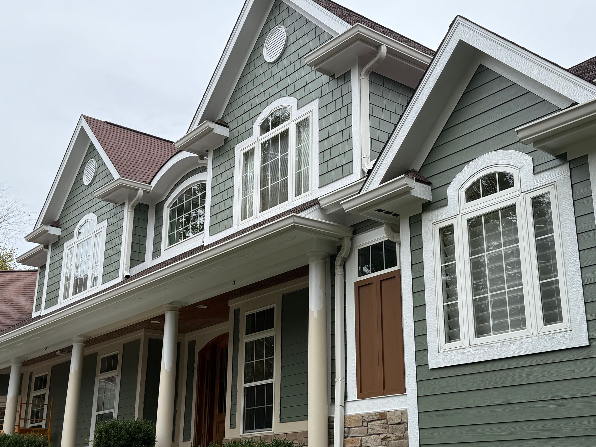 Gray townhouse row with white trim, arched windows, and brown front doors under a cloudy sky