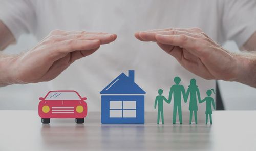 Hands shielding a toy car, house, and family figurines from above