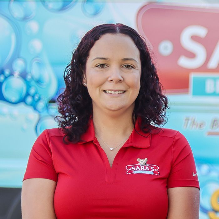 Woman in red polo shirt with Sara's logo, smiling in front of a van.