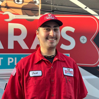 Man in red uniform smiles, standing in front of a service truck, wearing a baseball cap; company logo visible.