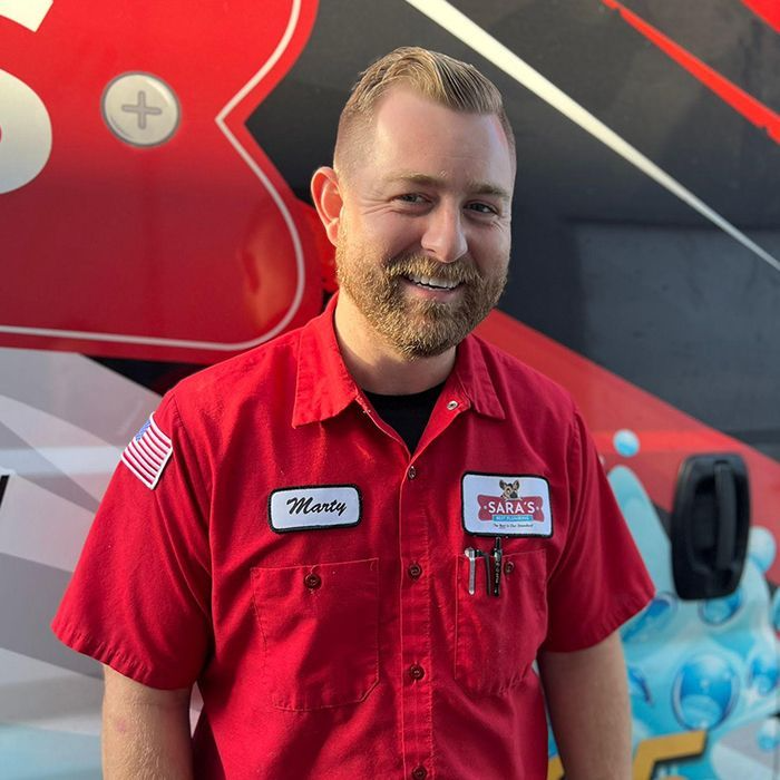 Marty in red work shirt with name tag, smiling in front of a red and white vehicle.