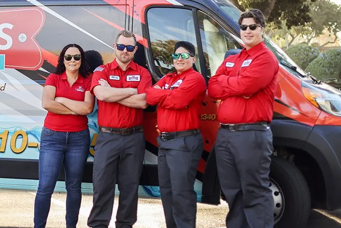 Four service technicians in red shirts and sunglasses stand confidently in front of a branded van.