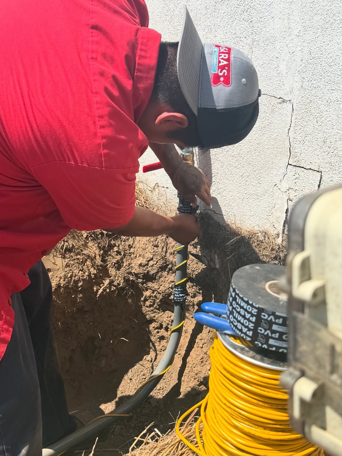 Man in red shirt working on buried electrical conduit, near a house.