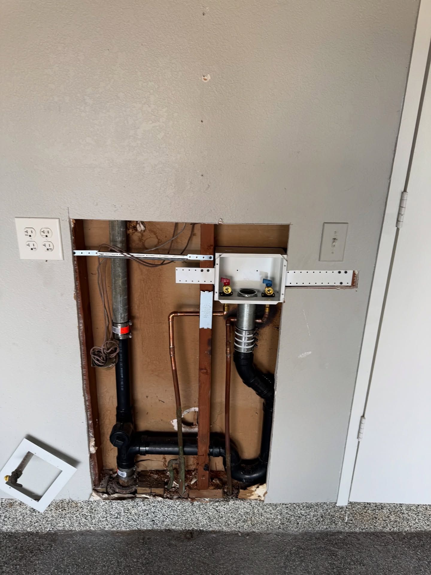 Plumbing and electrical in a wall cutout for a washing machine. Electrical outlets are visible on the left and right sides.