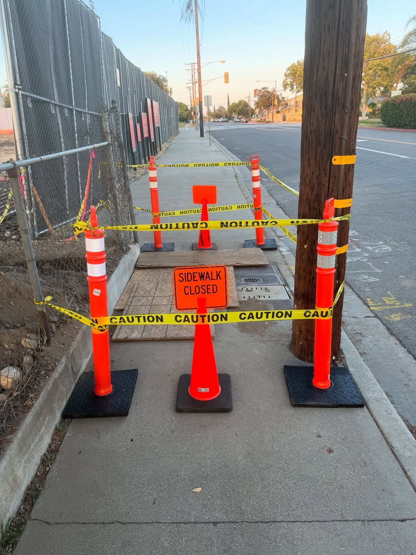 Sidewalk closed for construction: orange cones, caution tape, and a sign on a paved path.