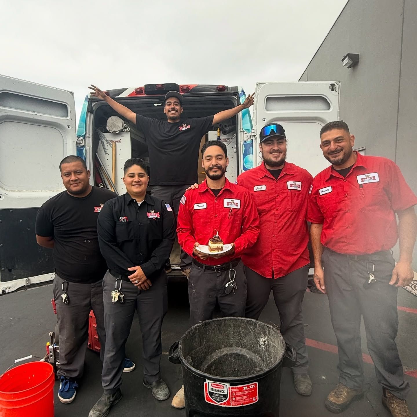 Group of service technicians smiling by their van, holding a cake and standing next to a bucket.