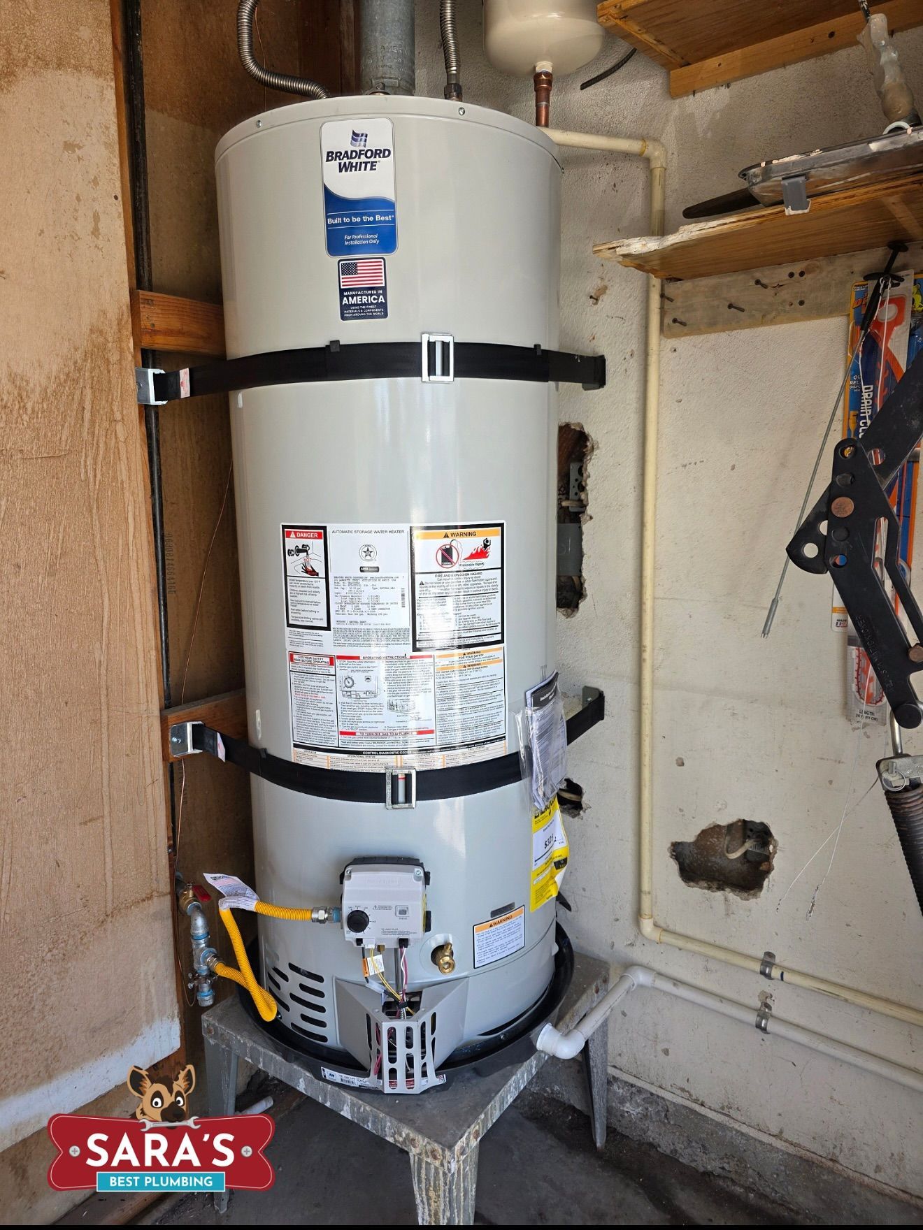 A tall, cylindrical water heater with black straps stands in a garage against a beige wall.