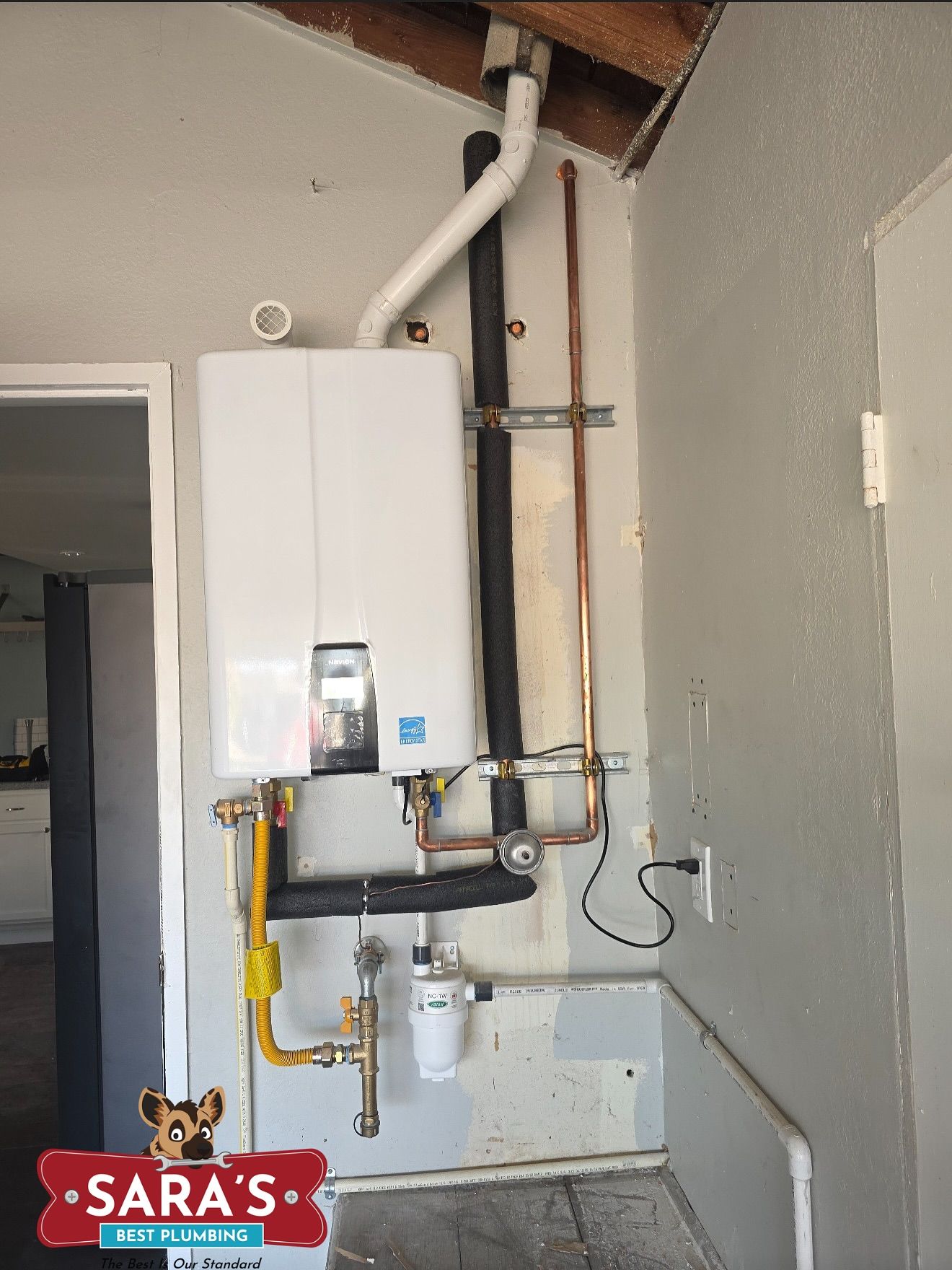 White tankless water heater mounted on a gray wall, with gas and water lines.