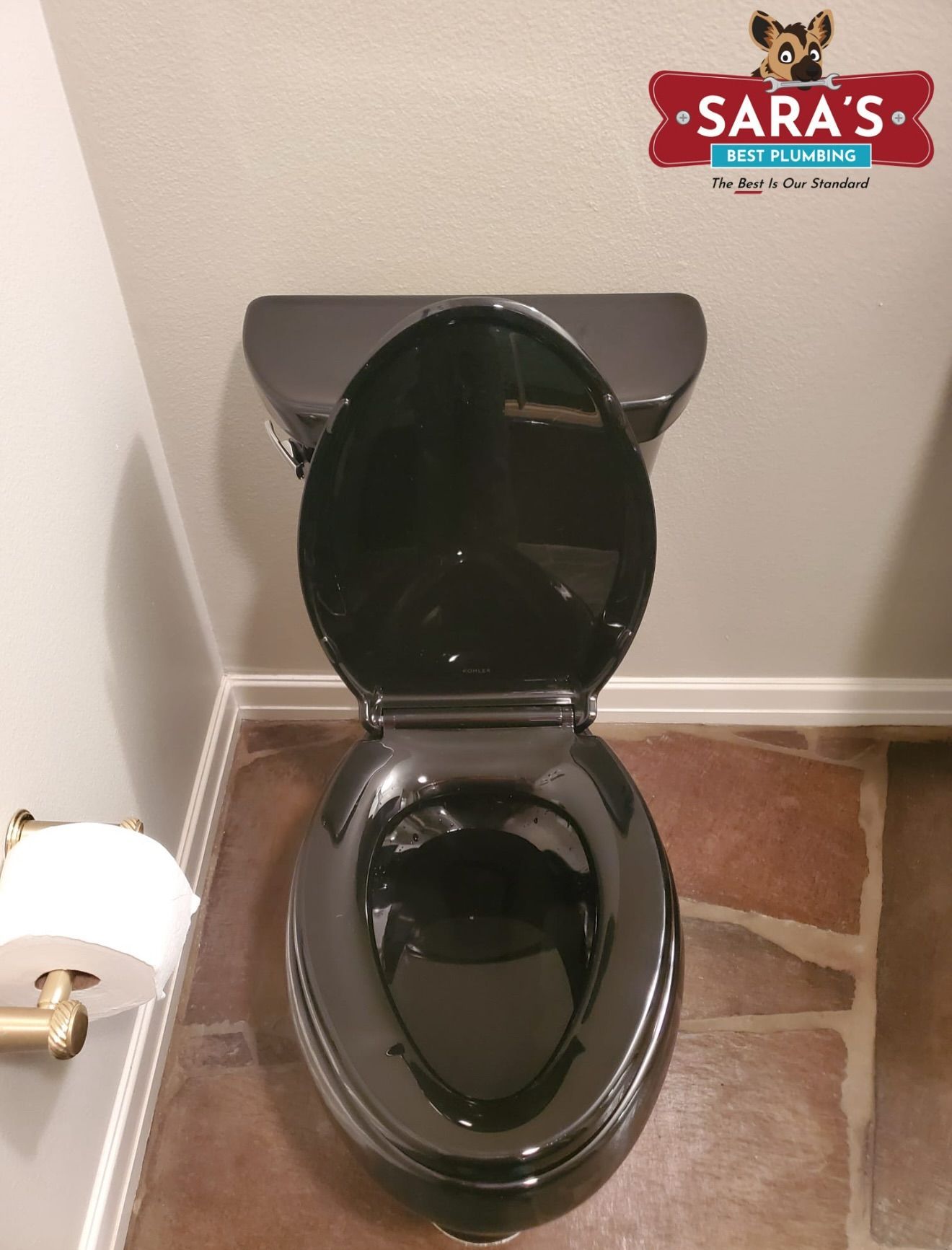 Black toilet with the lid open in a bathroom with brown flooring.