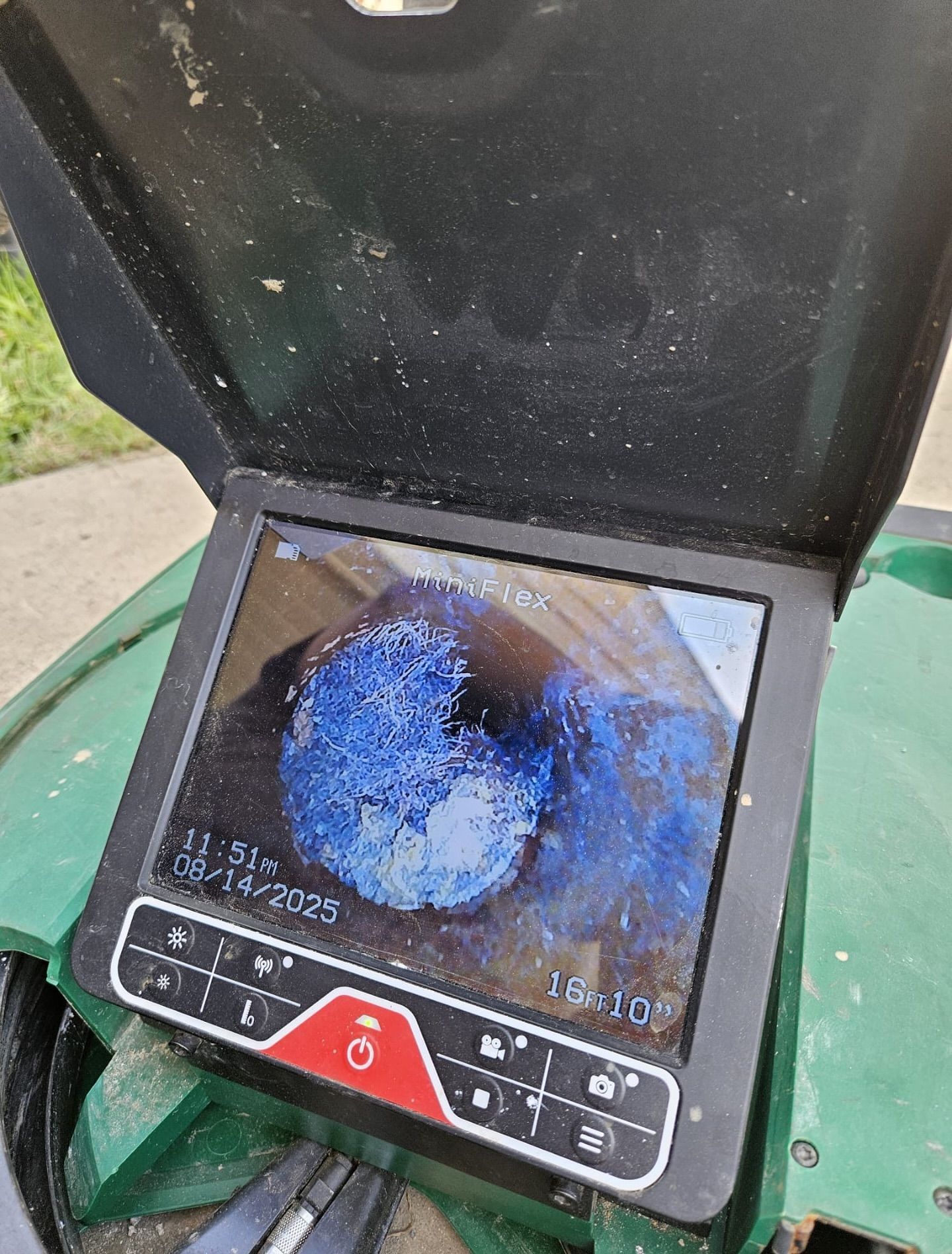 A camera screen displays a blue, round object. The screen is on a green machine outdoors.