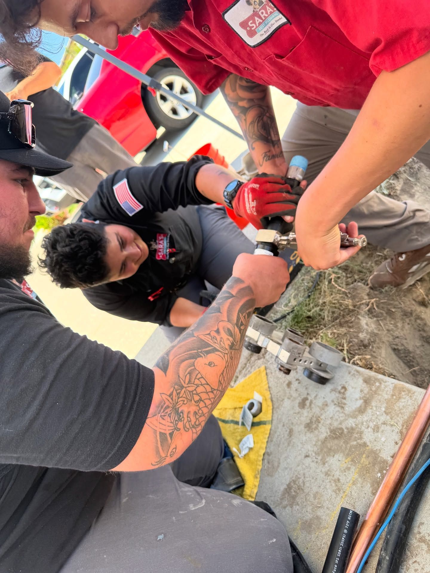Three men working on plumbing repairs outdoors. One holds a wrench.
