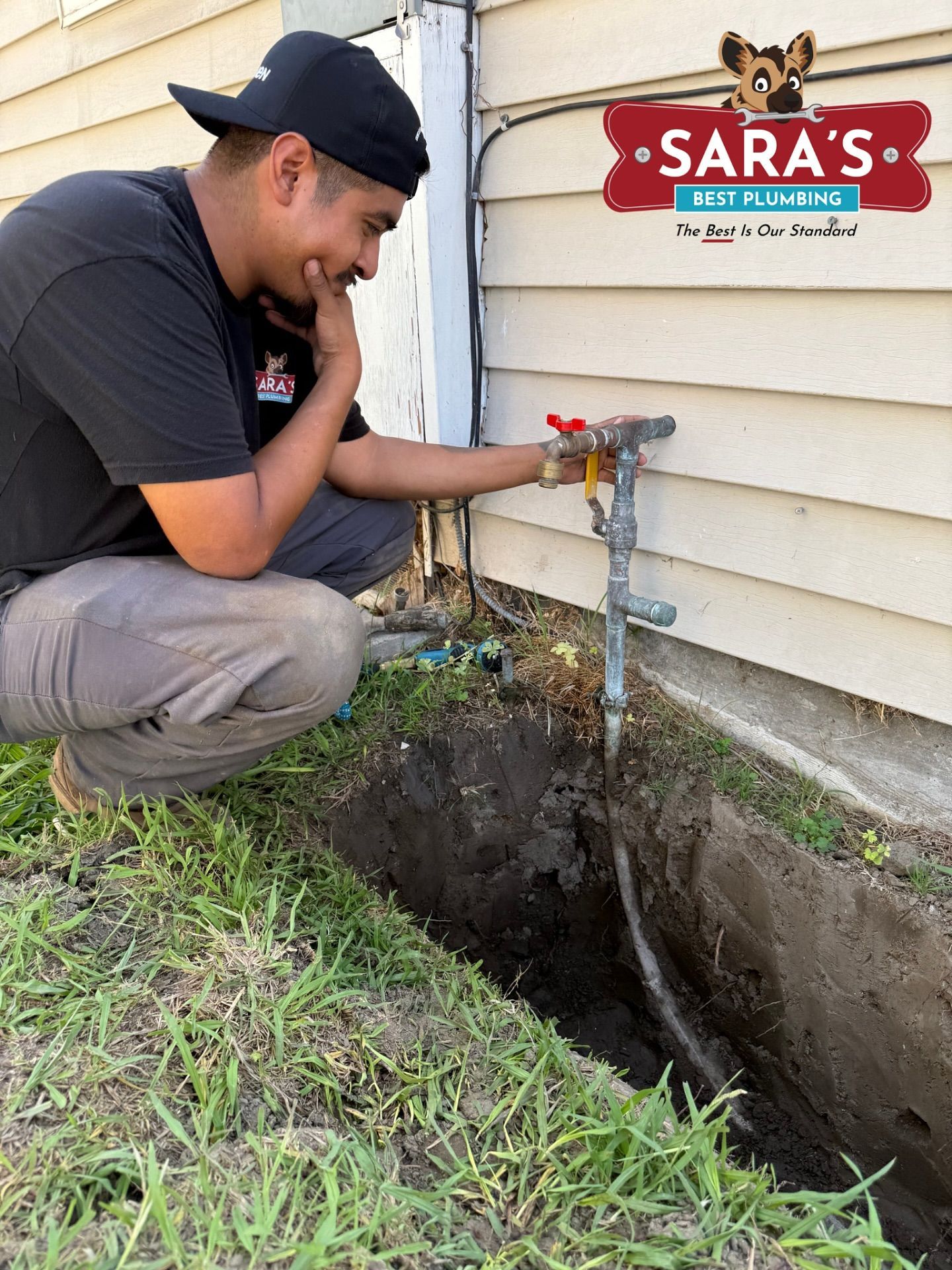 Man kneeling by gas line, looking at it in a trench.  House exterior, grass, and Sara's logo.