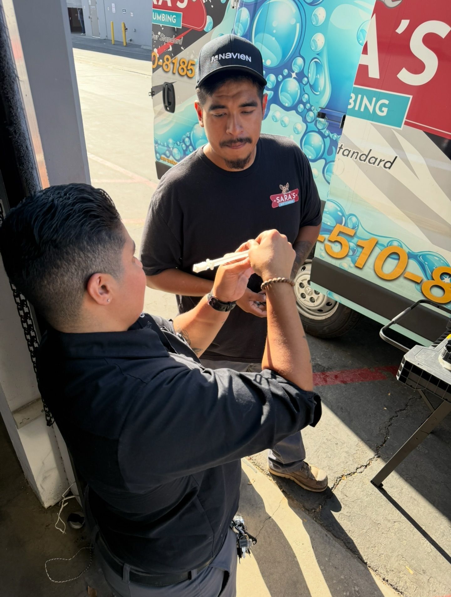 Two staff examining something outdoors near a cleaning van. One man holds up an item while the other observes.