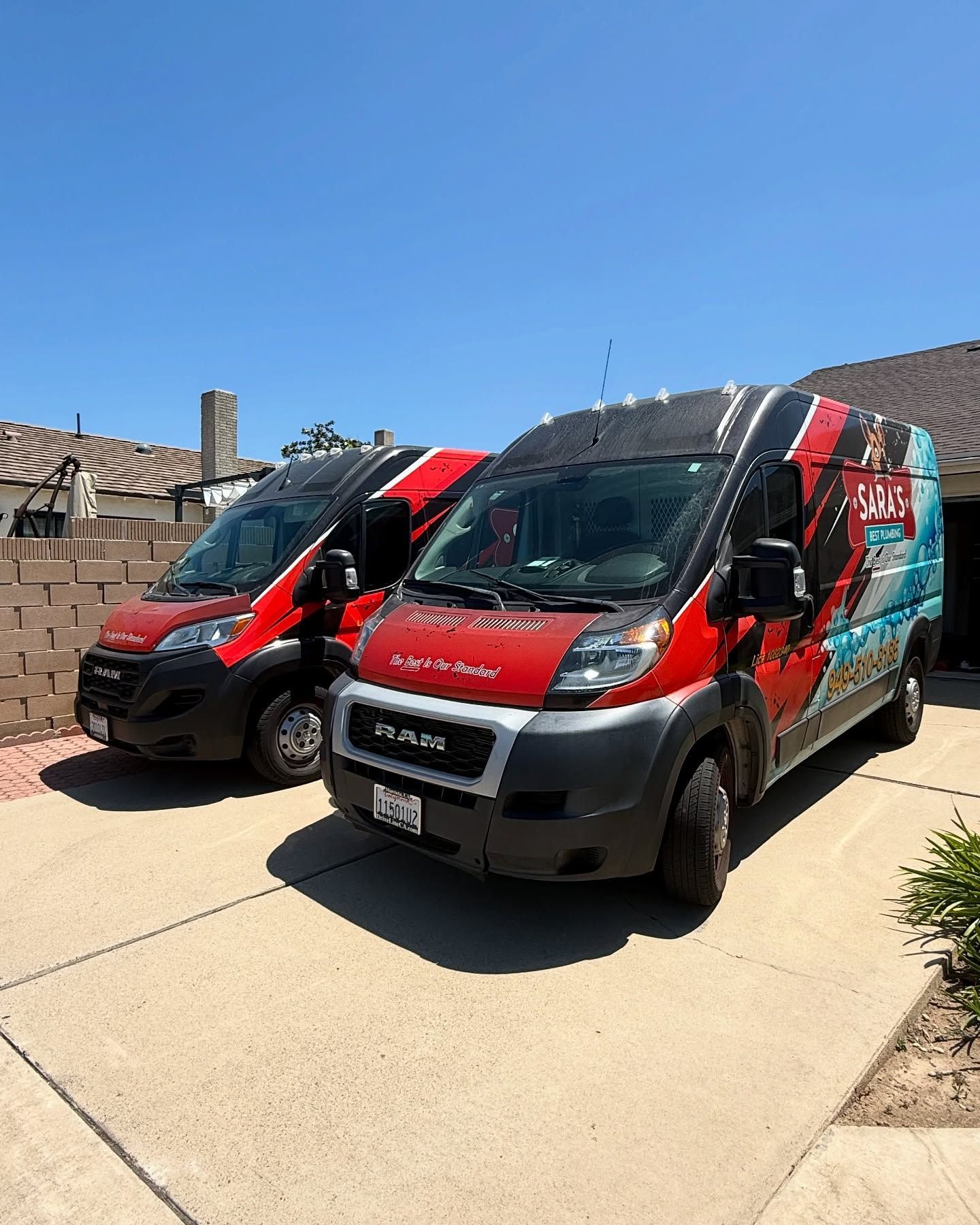 Two red and black vans parked in a driveway on a sunny day, with company logos.