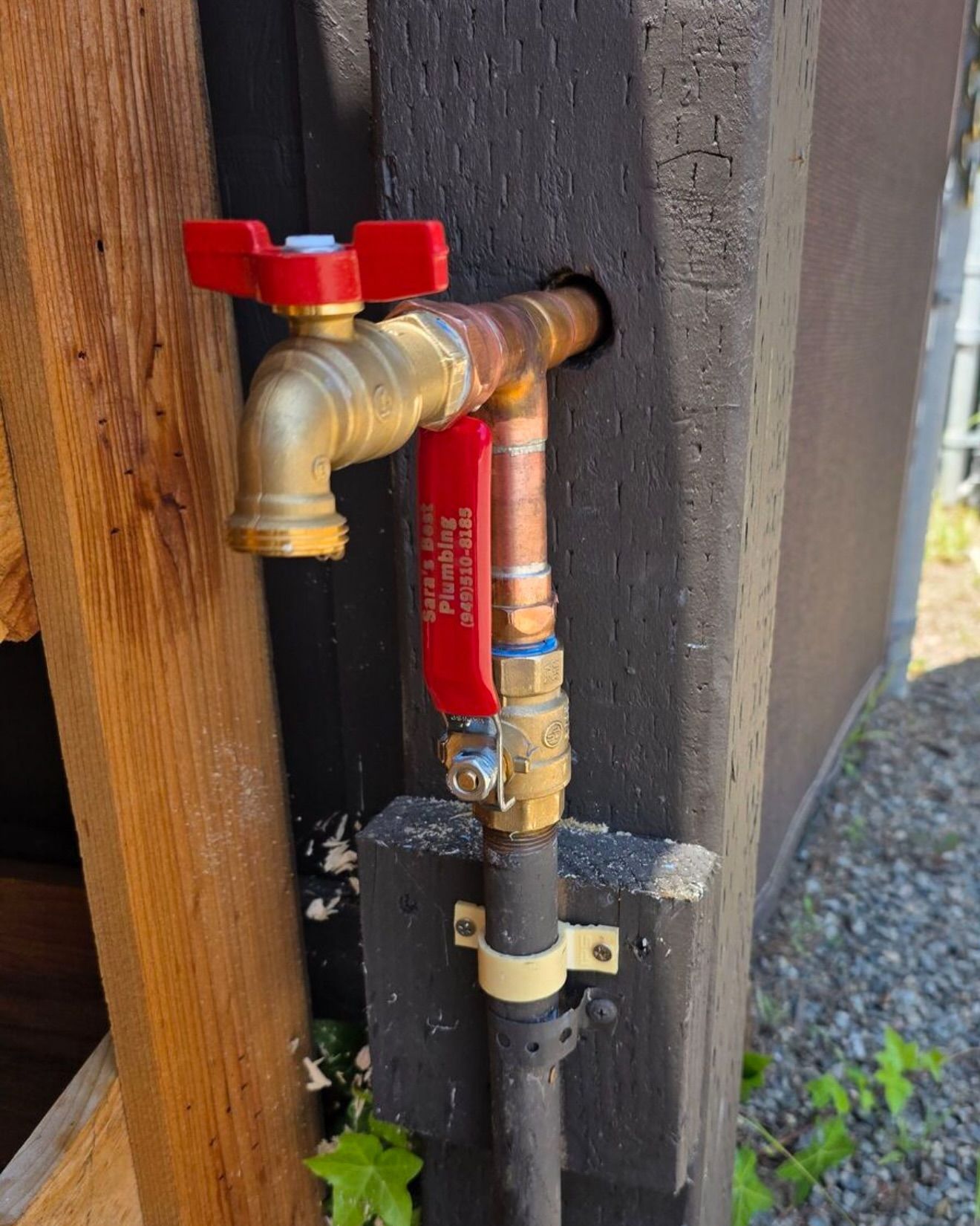 Outdoor water faucet with red handles, attached to a black wooden post.