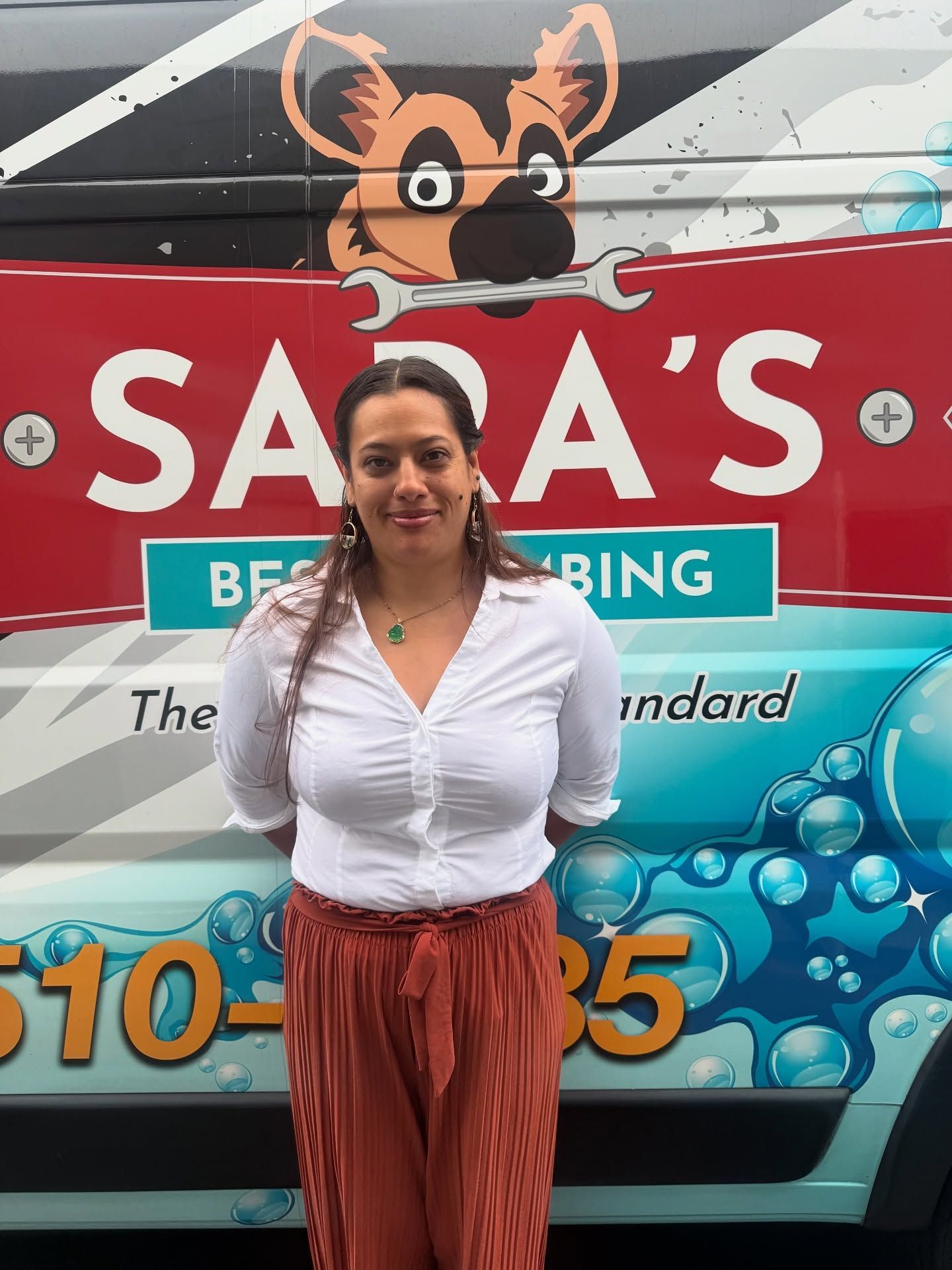 Woman in white shirt and orange pants stands in front of a van with 