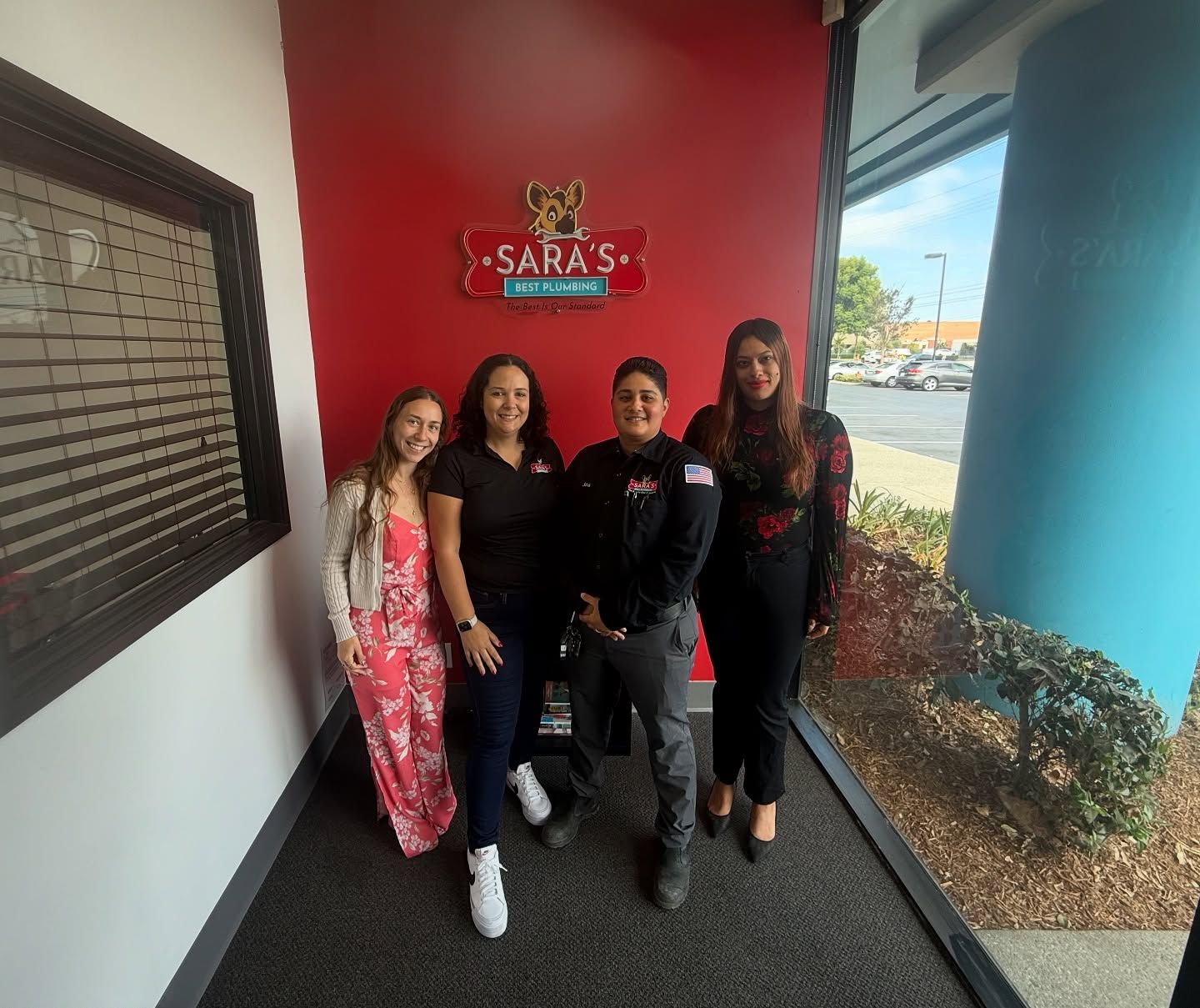 Four women standing near a red wall with 