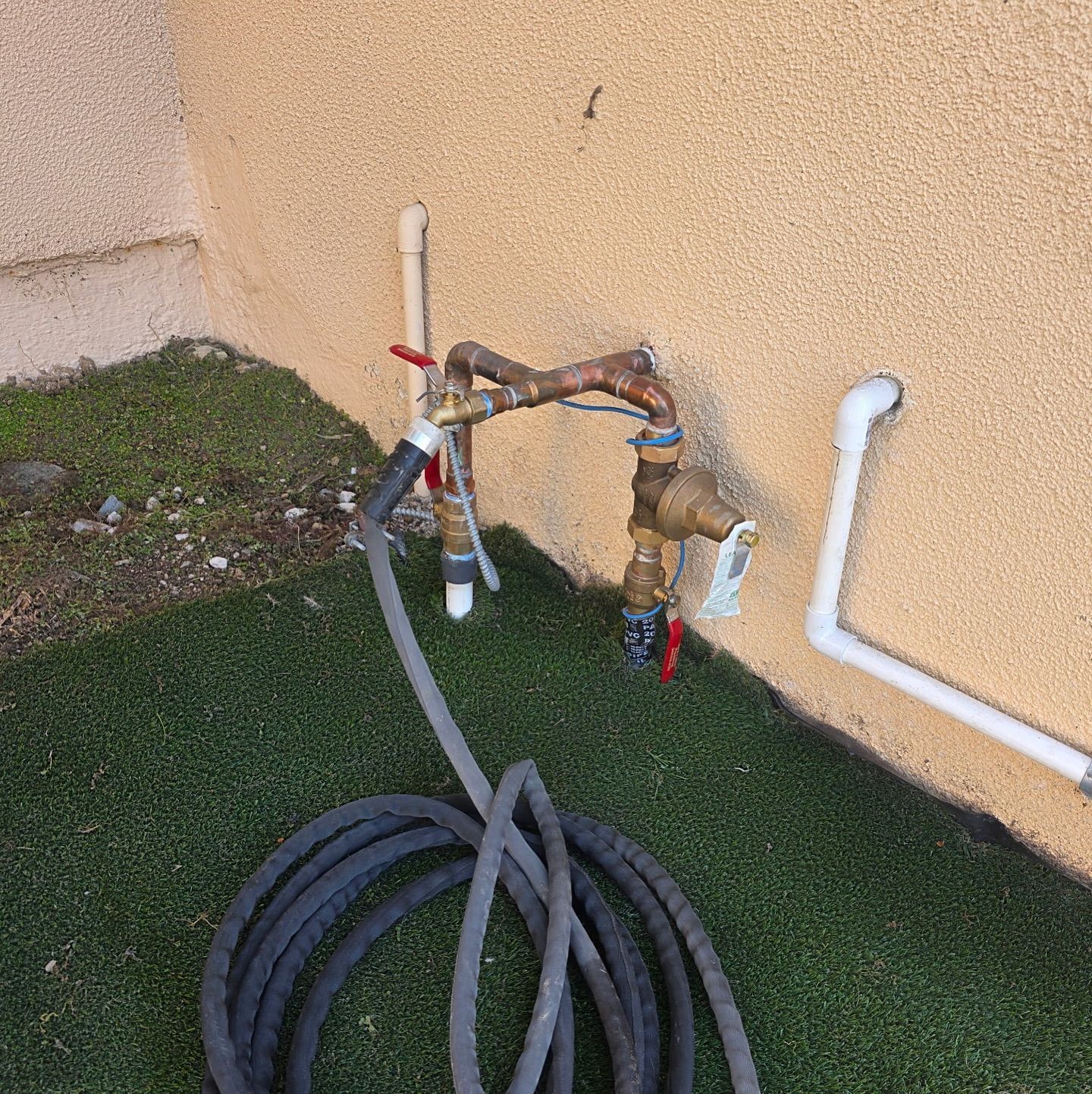 Copper pipes and hose connected to outdoor water faucet against stucco wall.