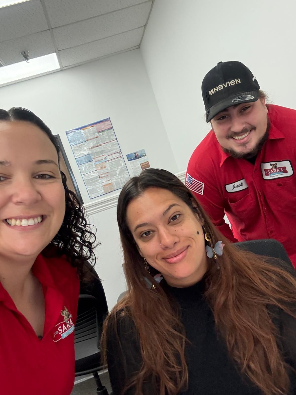 Three smiling people in red uniforms; indoors, posing for a selfie.
