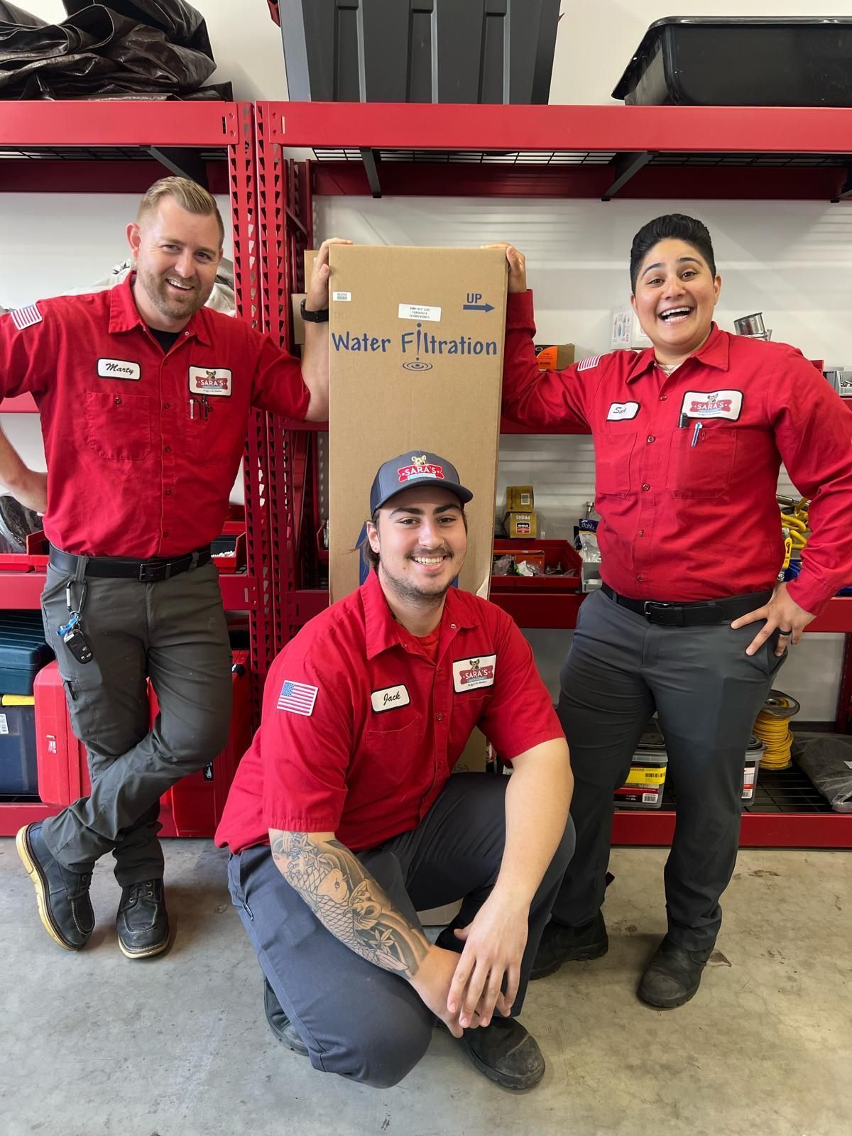 Three people in red shirts pose with a box in a shop.
