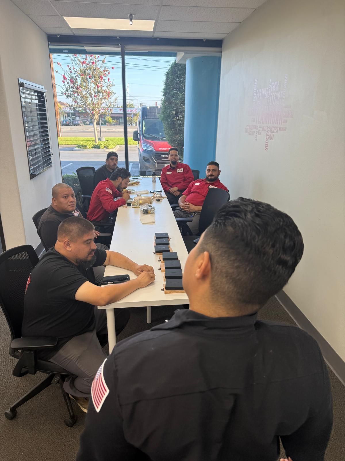 A group of men in red and black uniforms sit around a table in a conference room.