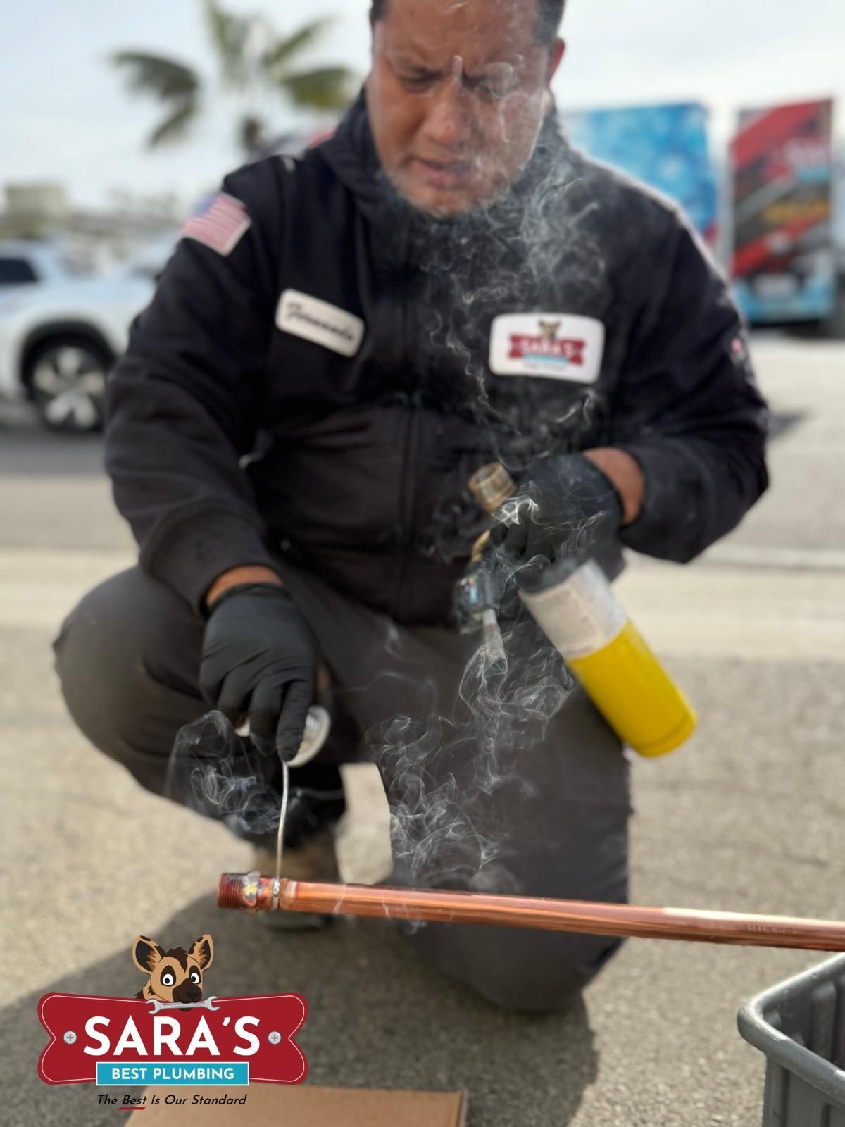 Plumber soldering copper pipe outside. He's kneeling, using a torch, with smoke rising.