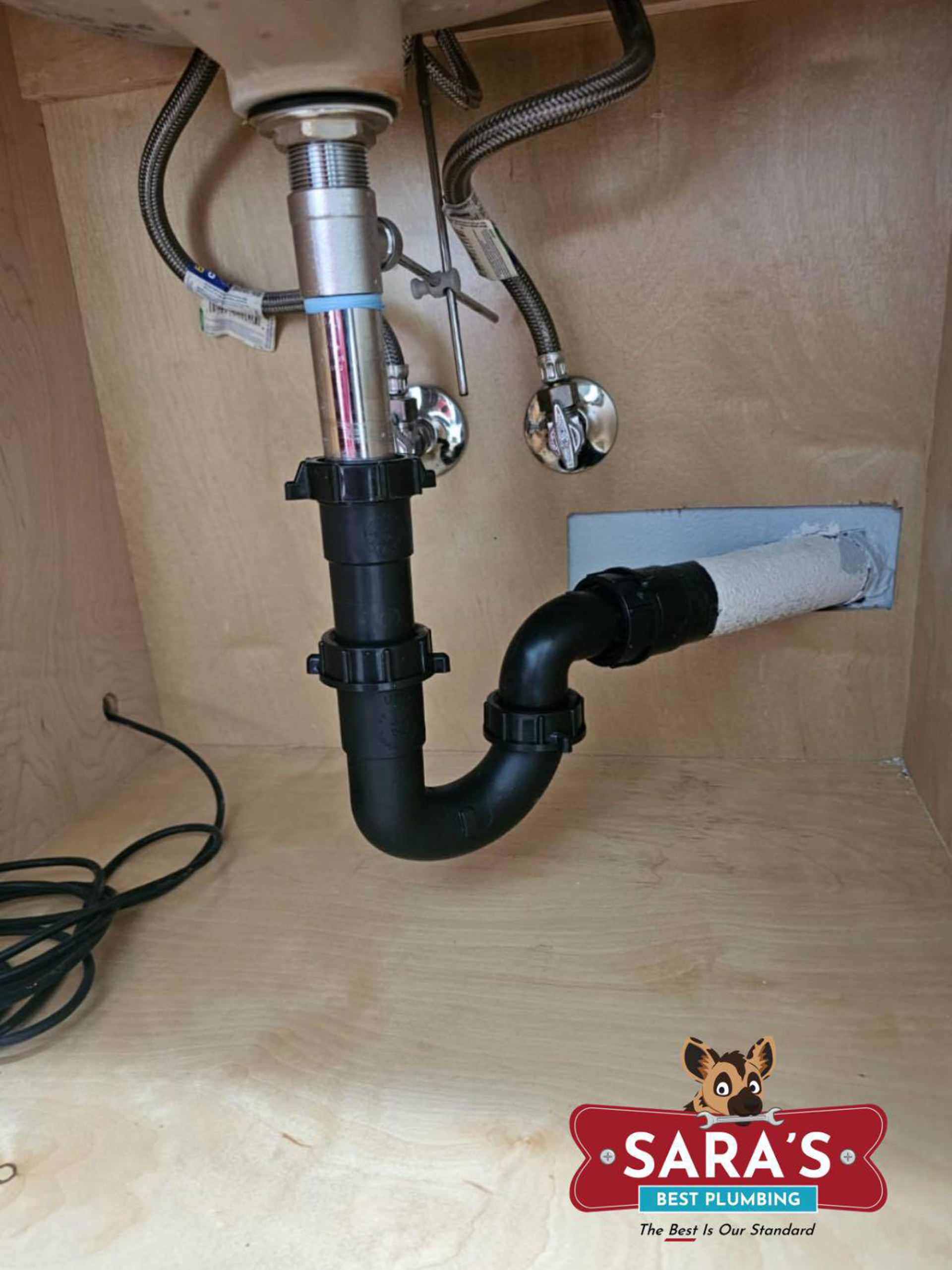 Under-sink plumbing with black p-trap, chrome pipes, and white wall drain