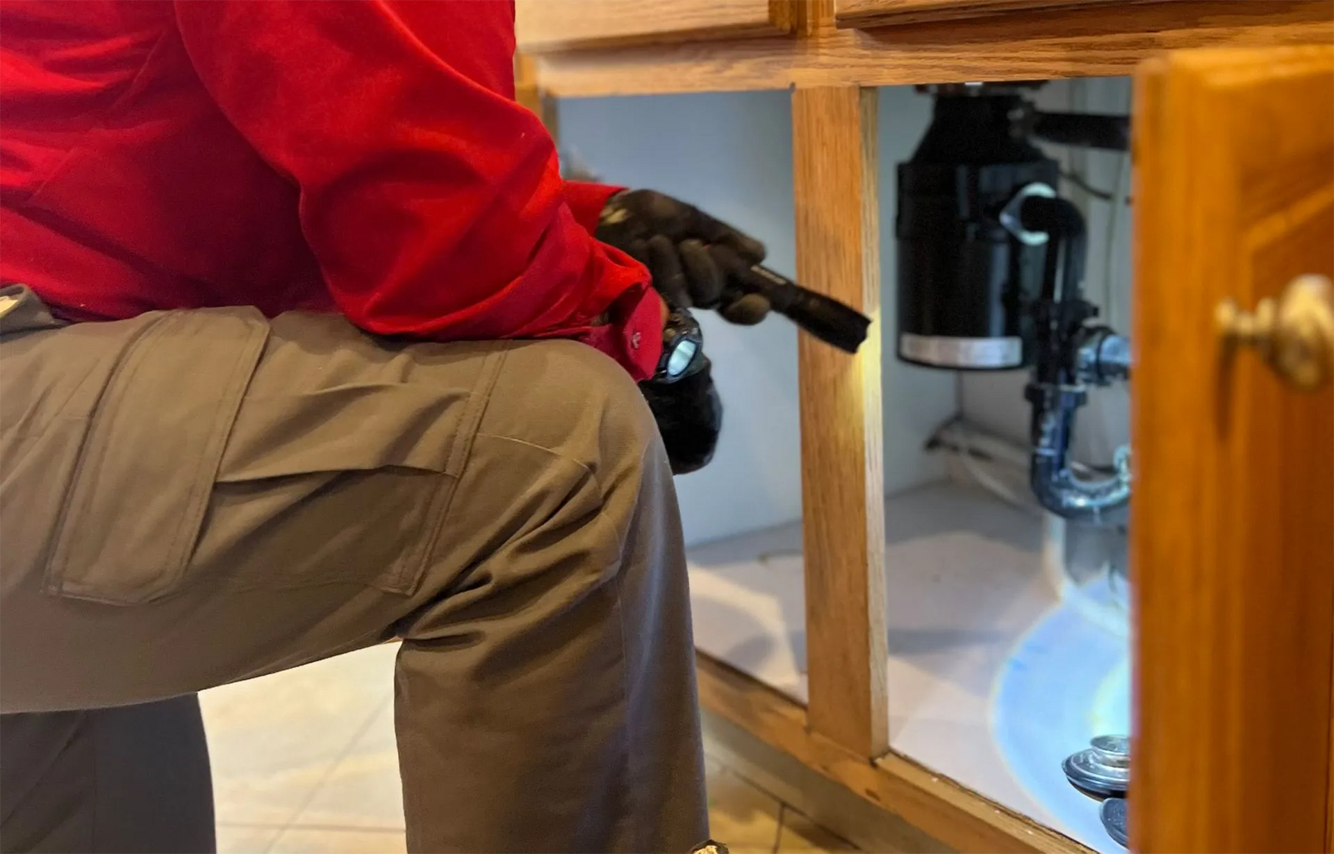 Person inspecting under kitchen sink with a flashlight