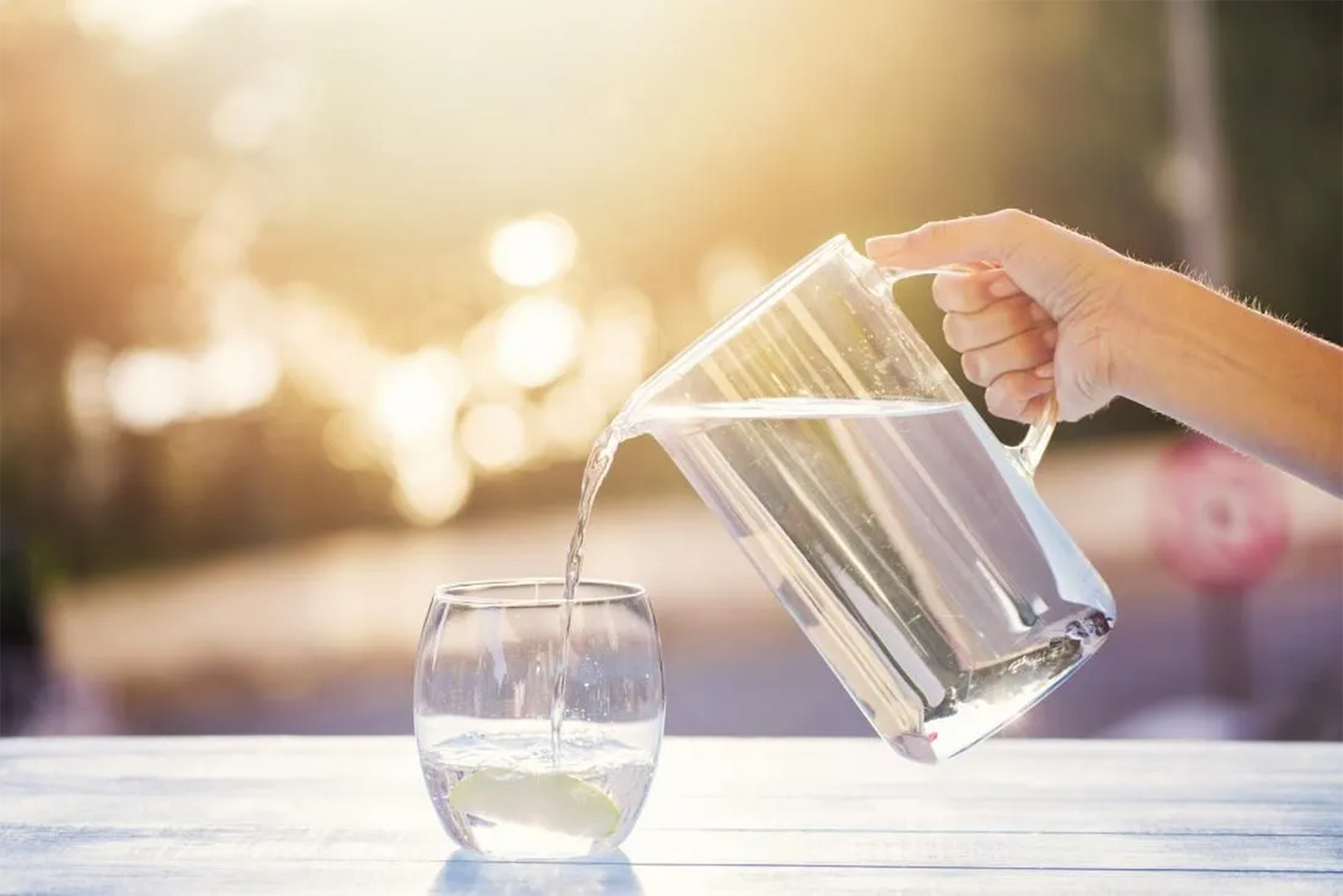 Hand pouring water from a pitcher into a glass on a table outdoors