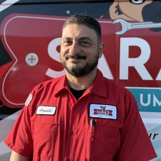 Woman in red polo shirt with Sara's logo, smiling in front of a van.