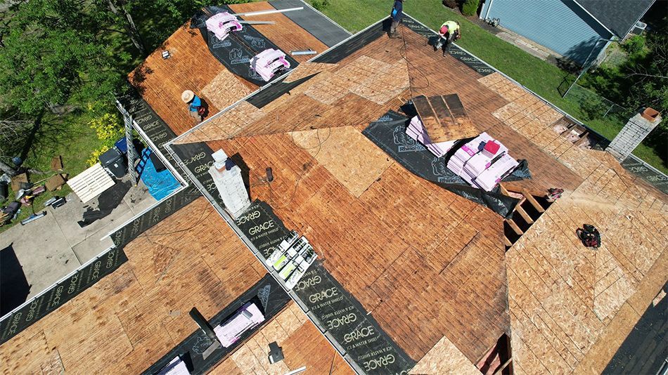 Aerial view of a damaged roof with tarps, missing shingles, and scattered debris after storm damage.