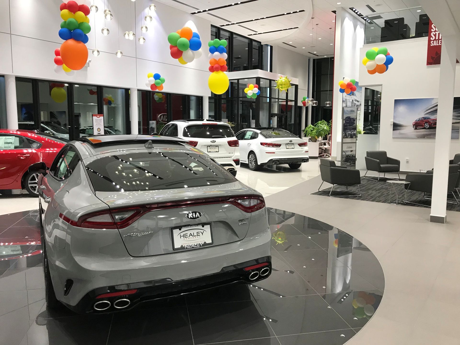Cars displayed in a bright showroom with colorful balloons hanging from the ceiling