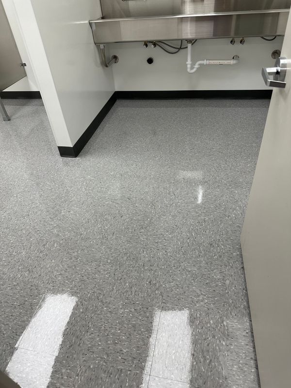Empty stainless-steel kitchen area with gray speckled floor and wall-mounted counter.