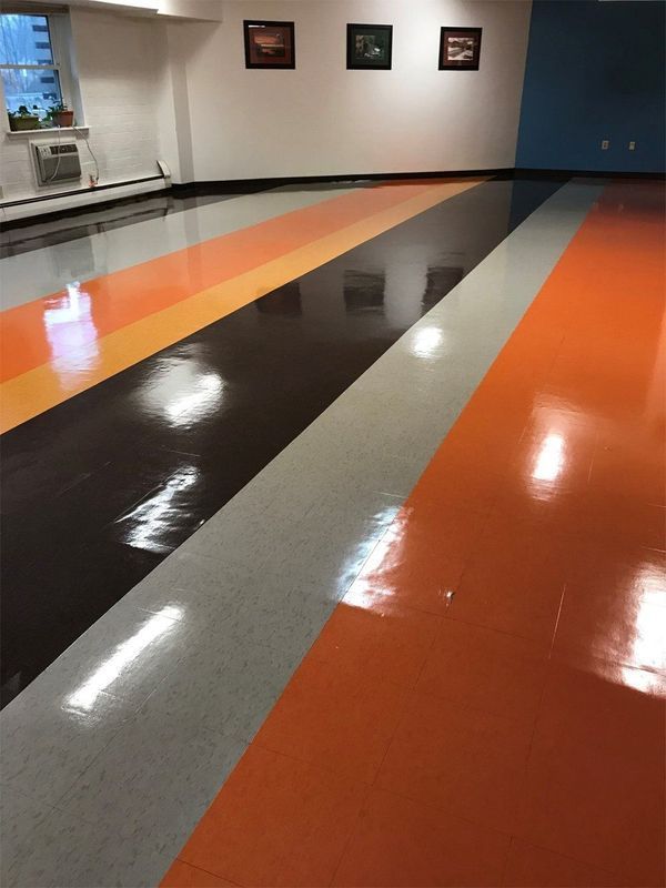 Shiny striped floor in orange, gray, and dark brown inside an empty room with wall art.