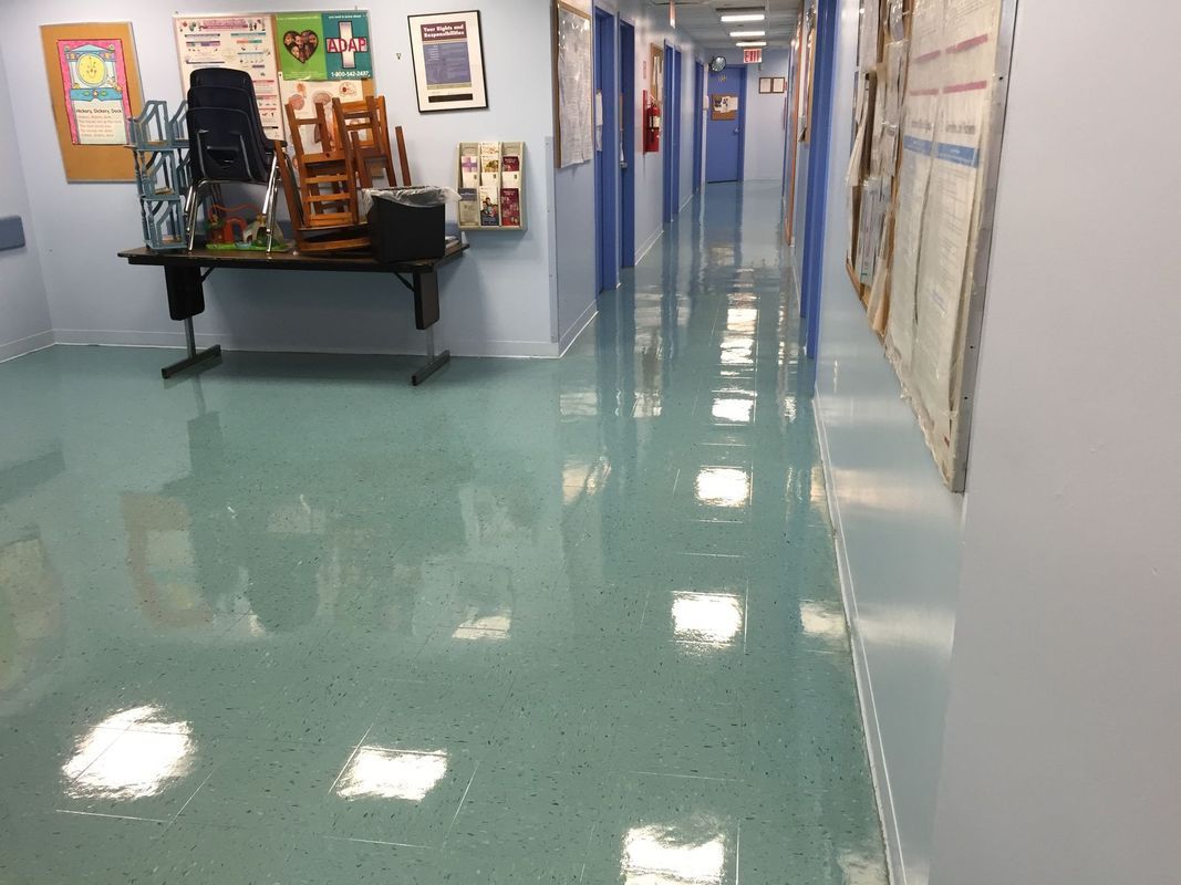 Empty school hallway with shiny blue floor, desks and chairs along the left wall, and doors on the right.