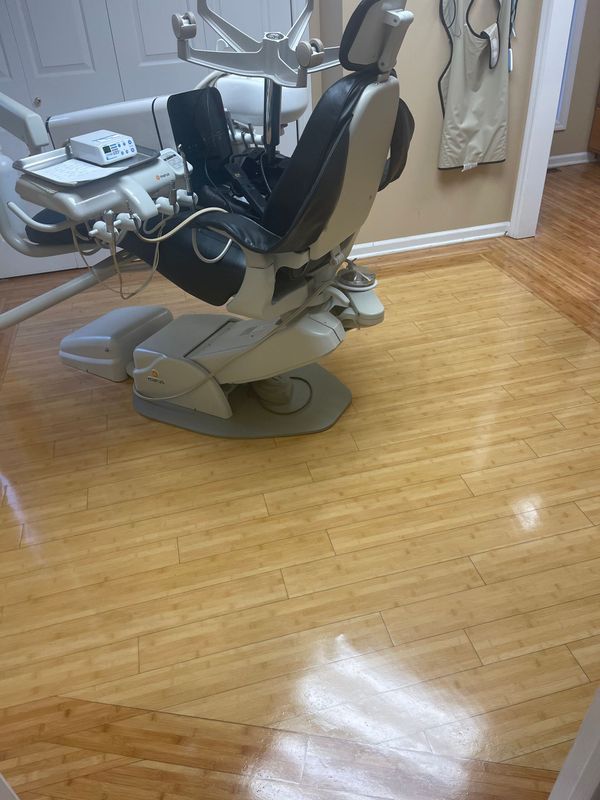 Dental treatment chair and equipment in a clinic room with a wood floor and mirrored wall.
