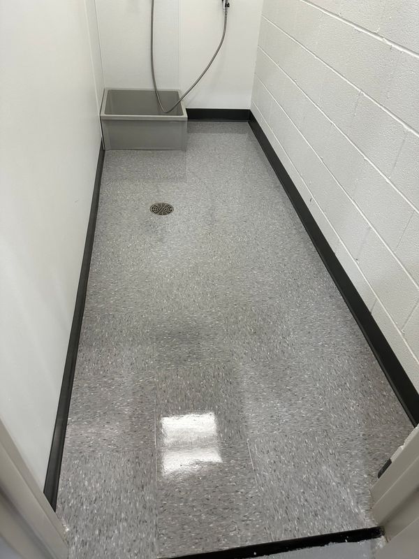 Narrow gray utility shower room with a drain, wall-mounted fixture, and cinder block walls
