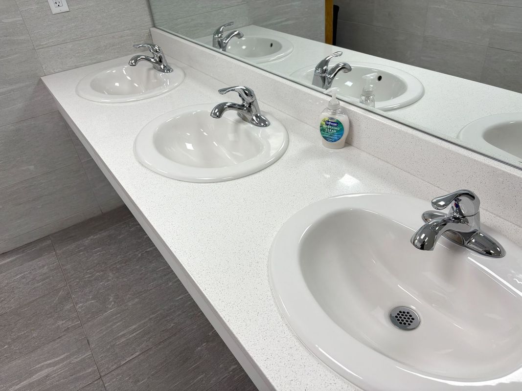 Row of white sinks and chrome faucets in a clean restroom with a wall mirror