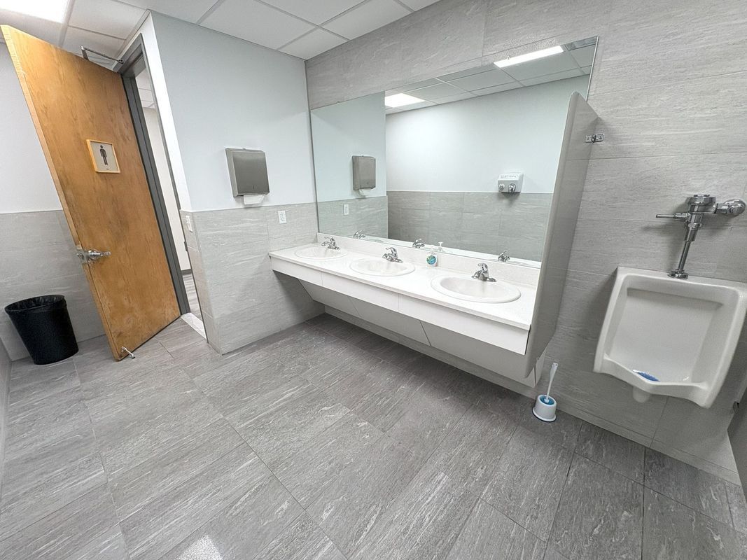Accessible restroom with sinks, mirror, wall-mounted dispenser, and urinal on gray flooring
