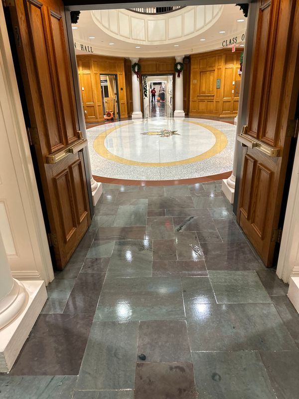 Open double doors to a bright marble foyer with a circular inlaid floor and wood-paneled walls