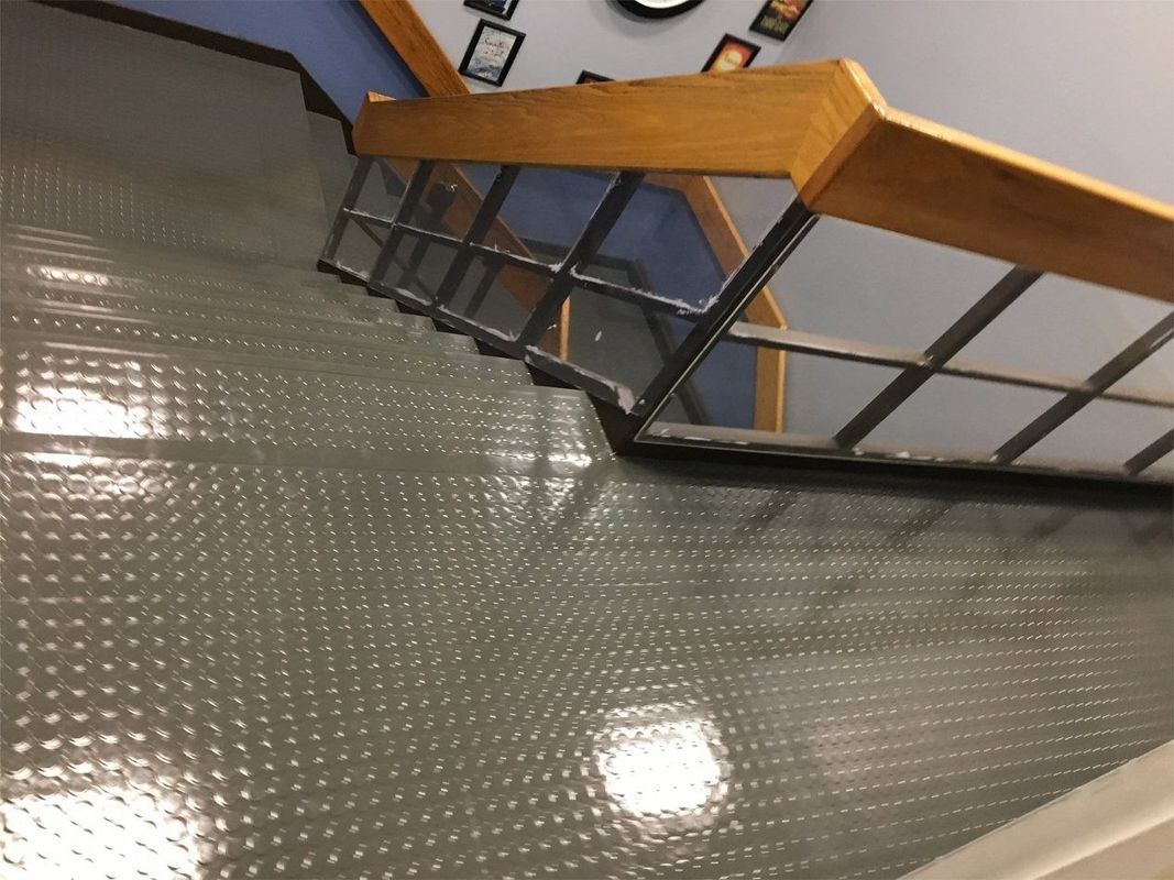Metal stair railing with wooden handrail over a gray textured floor in an indoor hallway