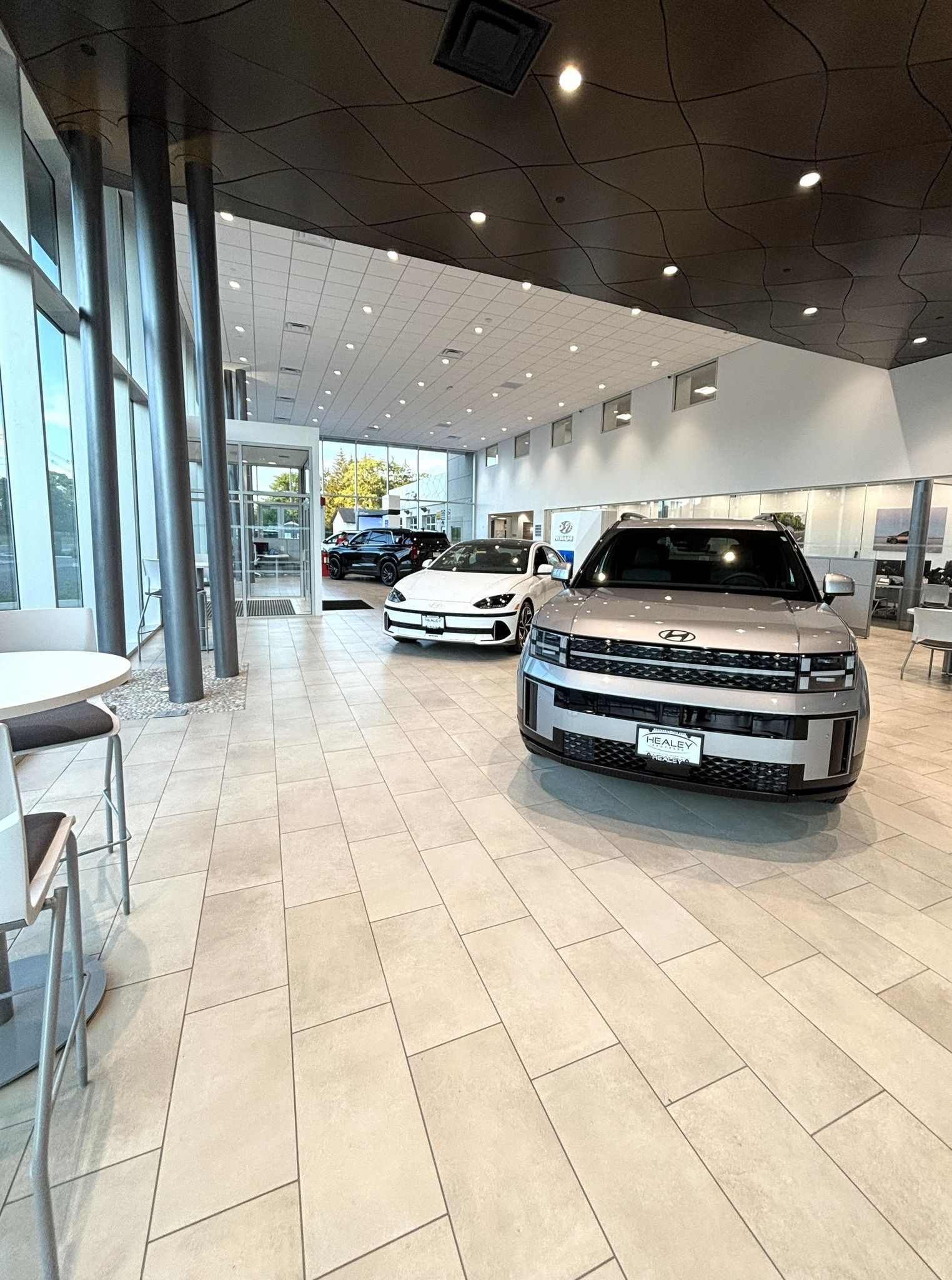 Car showroom with several parked cars under bright ceiling lights and tiled floors