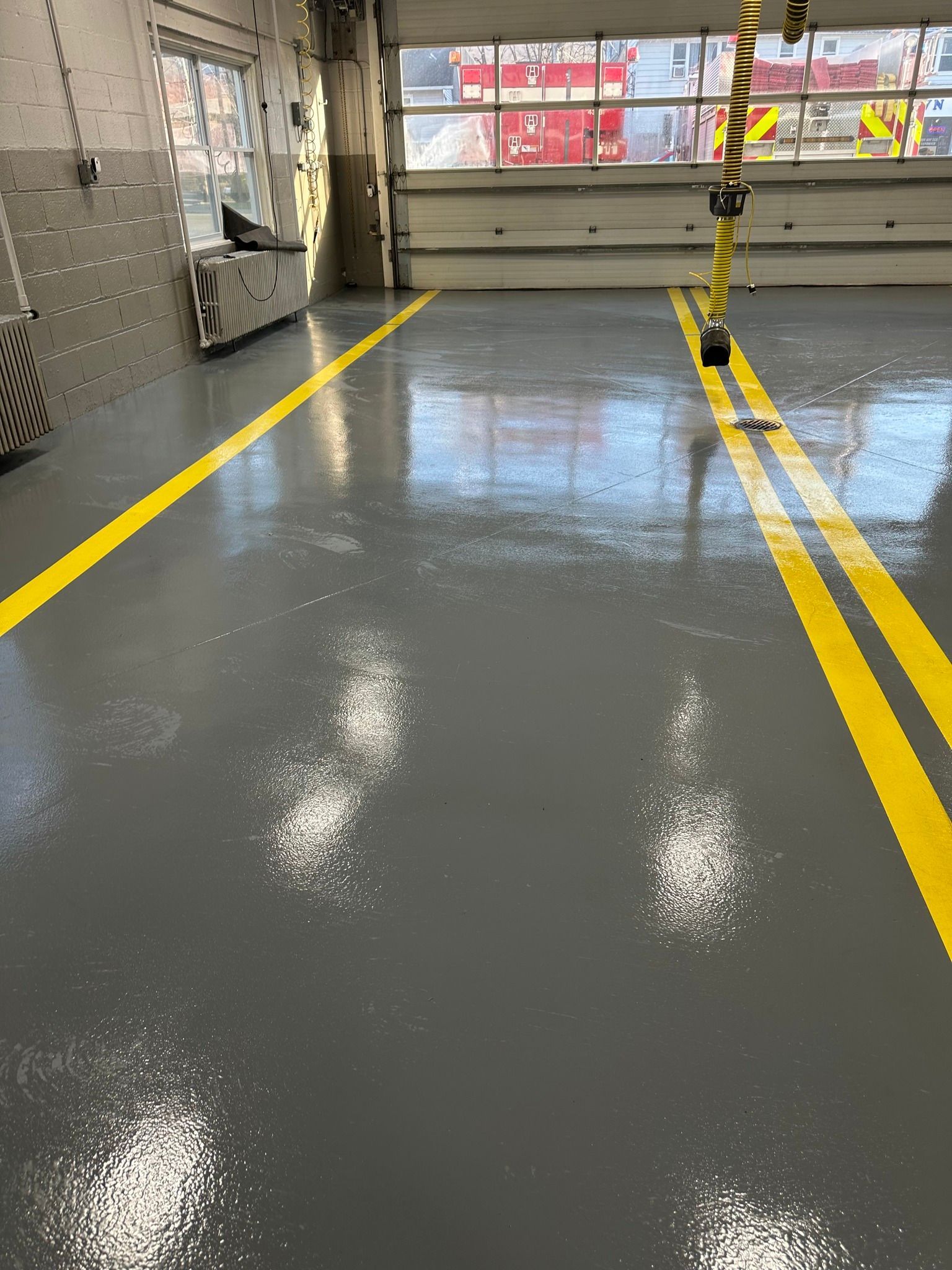Glossy gray floor in an industrial hallway with yellow safety lines and black-yellow striped post near a garage door