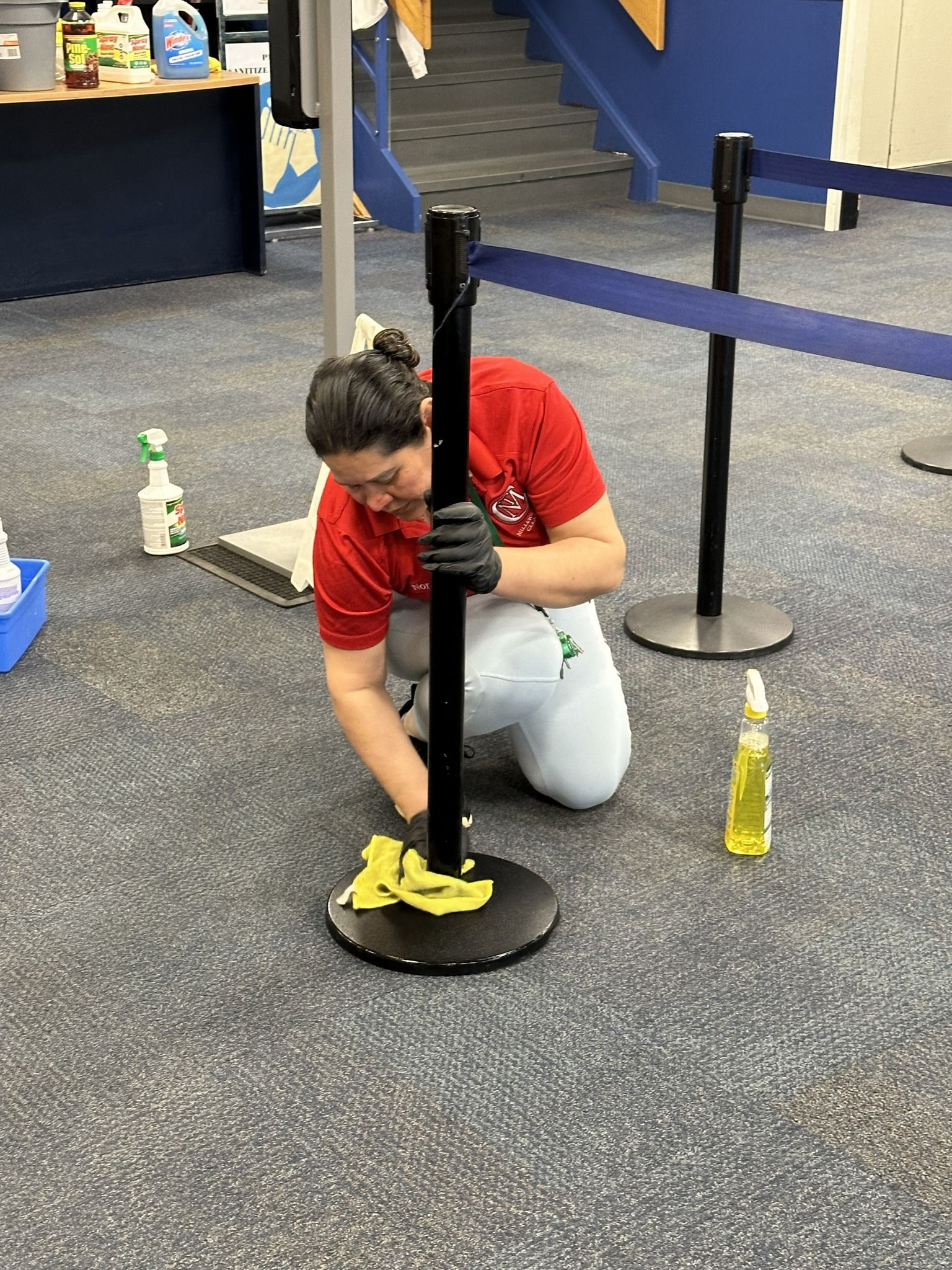 Person kneeling on a carpeted floor, assembling a black stanchion post with yellow caution tape nearby.