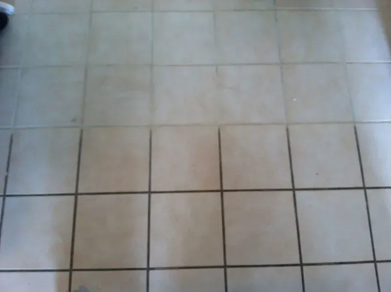 Close-up of a beige tiled floor with dark grout lines and a shadowed left edge